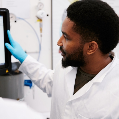 A male student in a lab coat wearing gloves