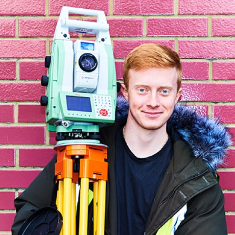 male student holding surveying equipment