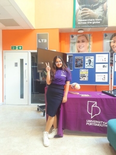 International student Anuja standing in front of a purple clothed table at the information fair